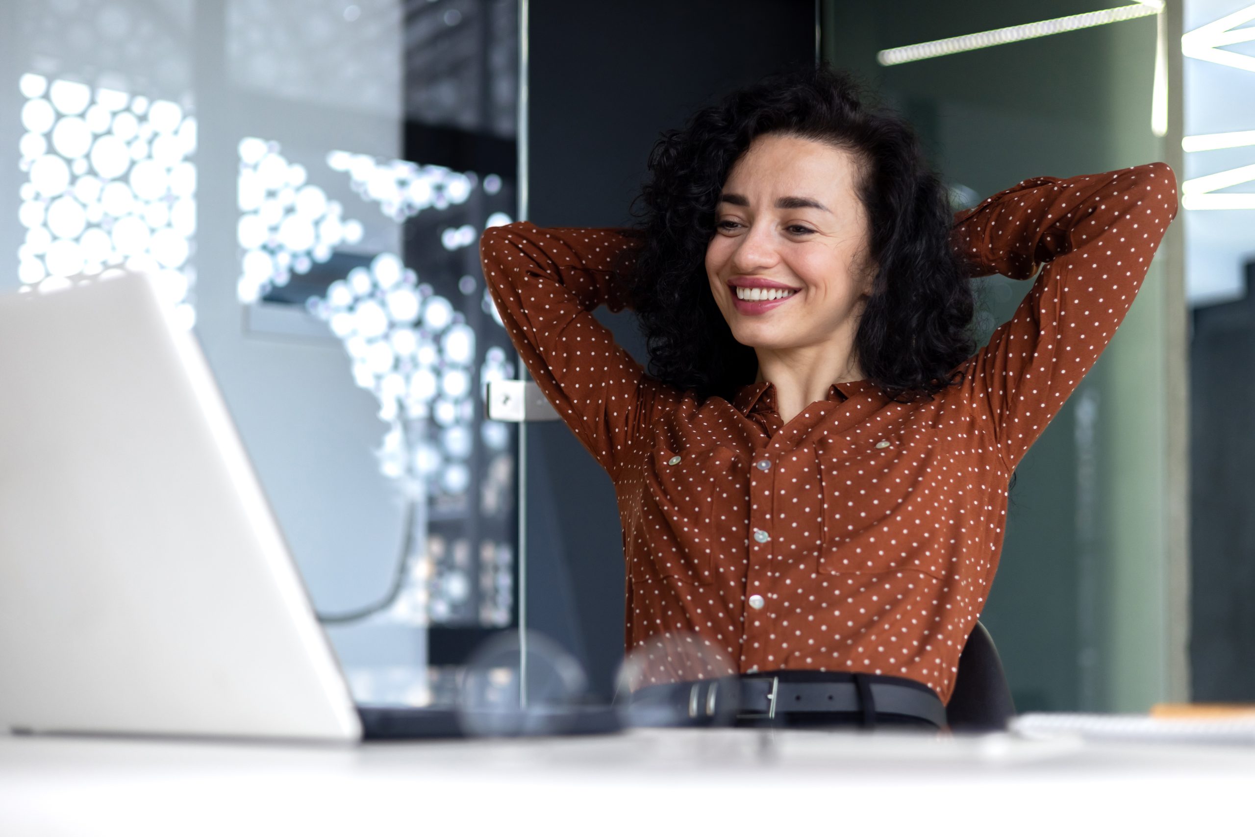 Happy thinking woman at workplace inside office, business woman with hands behind head completed work well, latin american woman satisfied with achievement results looking at laptop screen